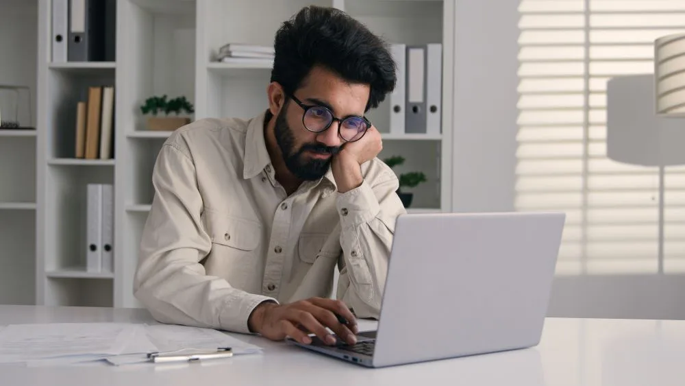 Disengaged employee looking bored at their desk, highlighting the effects of low employee engagement in the workplace